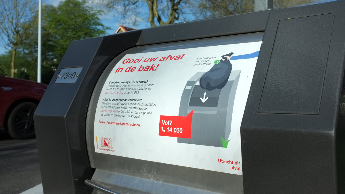De klep van een ondergrondse afvalcontainer, met daarop een uitleg van hoe de bak werkt en informatie over hoe je de gemeente Utrecht kunt bereiken via telefoon en internet